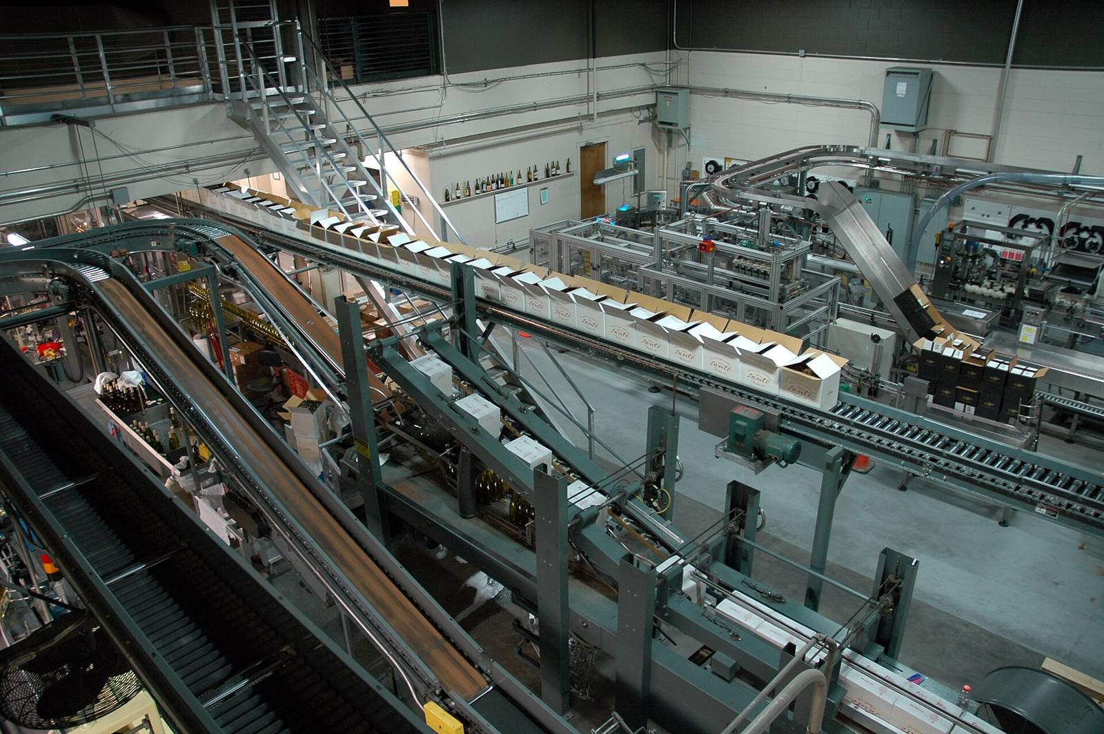 Una línea automatizada de embotellado y transportadores funcionando en una planta, vista desde arriba.